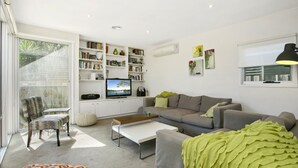Ein modernes Wohnzimmer mit einem grauen Sofa, einem weißen Couchtisch und einem Fernseher auf einem weißen Schrank. Bücherregale sind mit Büchern und Dekoration gefüllt.