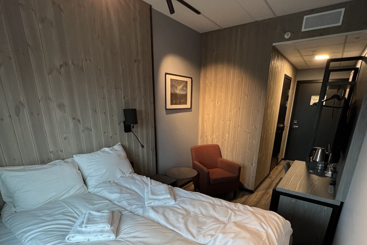 A hotel room with a large bed, a chair, a small table, a mirror, and a picture on the wall.