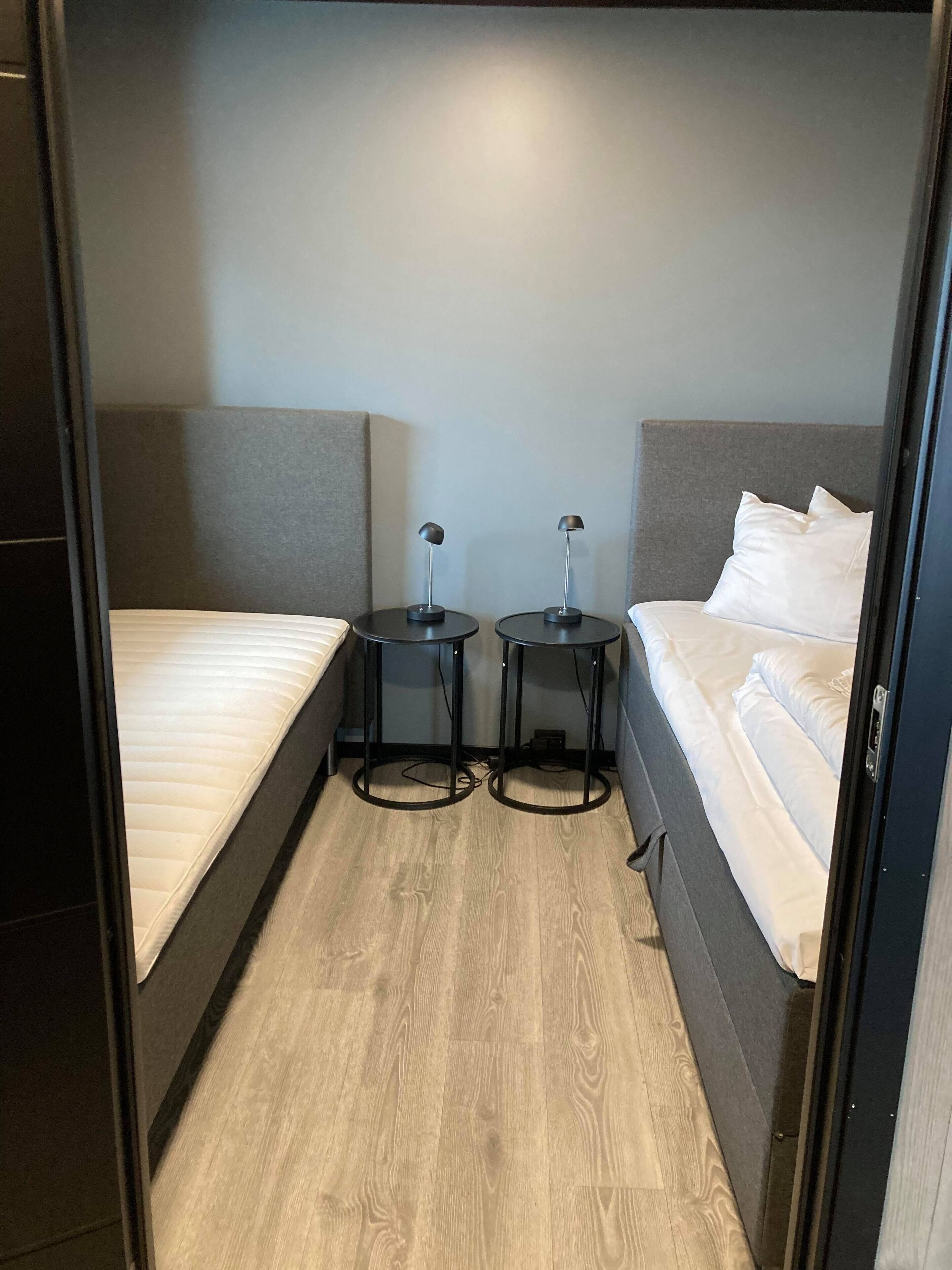 A compact hotel room with two single beds, a small table between them, and a door leading to another room.
