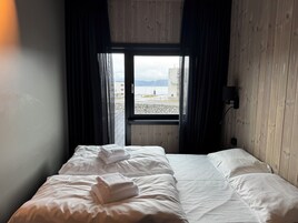 A hotel room with a bed, a window with curtains, and a view of a beach and buildings.