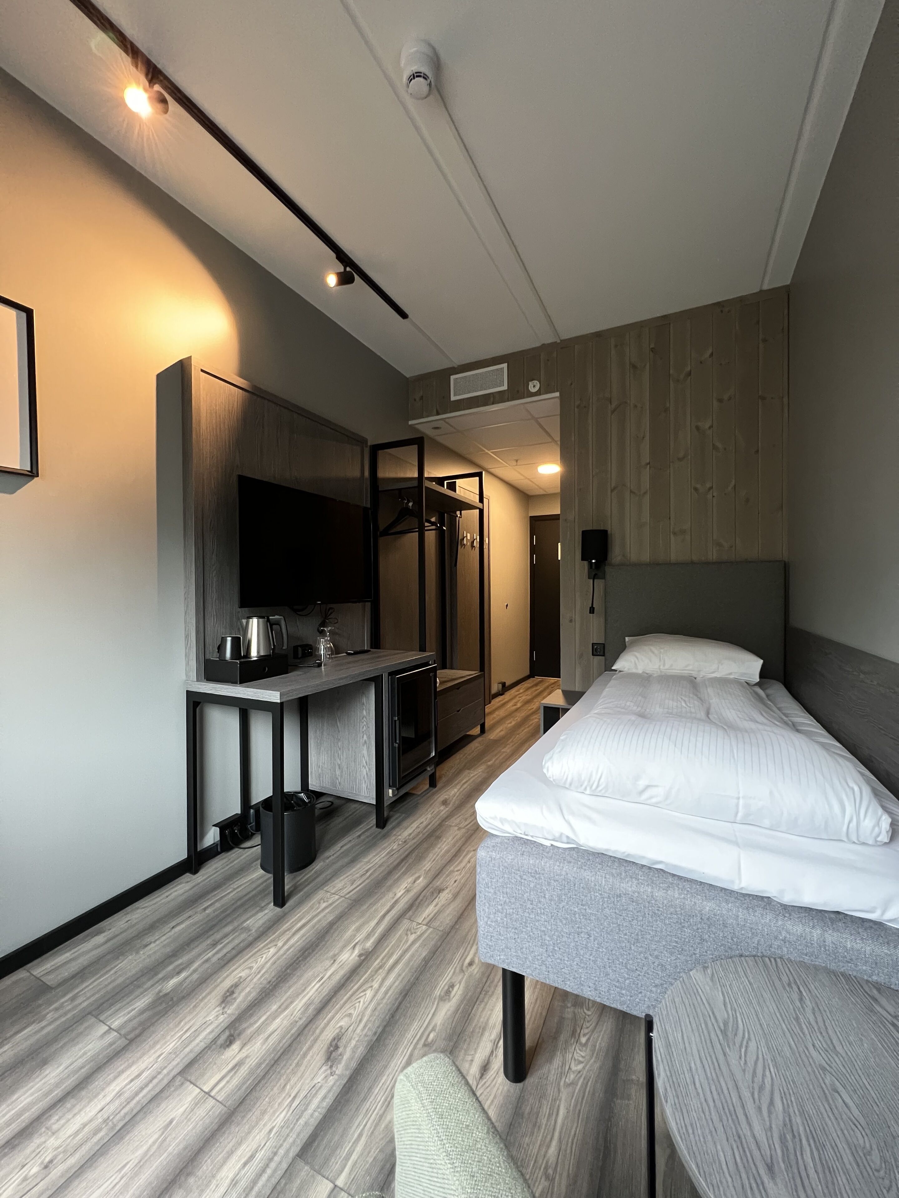 Una habitación de hotel moderna con cama, escritorio con televisor de pantalla plana, espejo y armario.