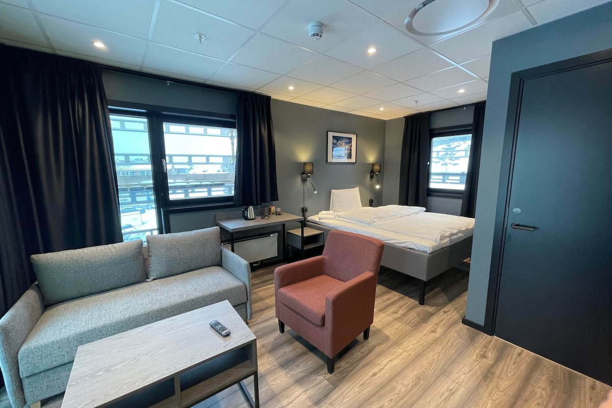 A modern hotel room with a bed, a sofa, a chair, a desk, and a small table.
