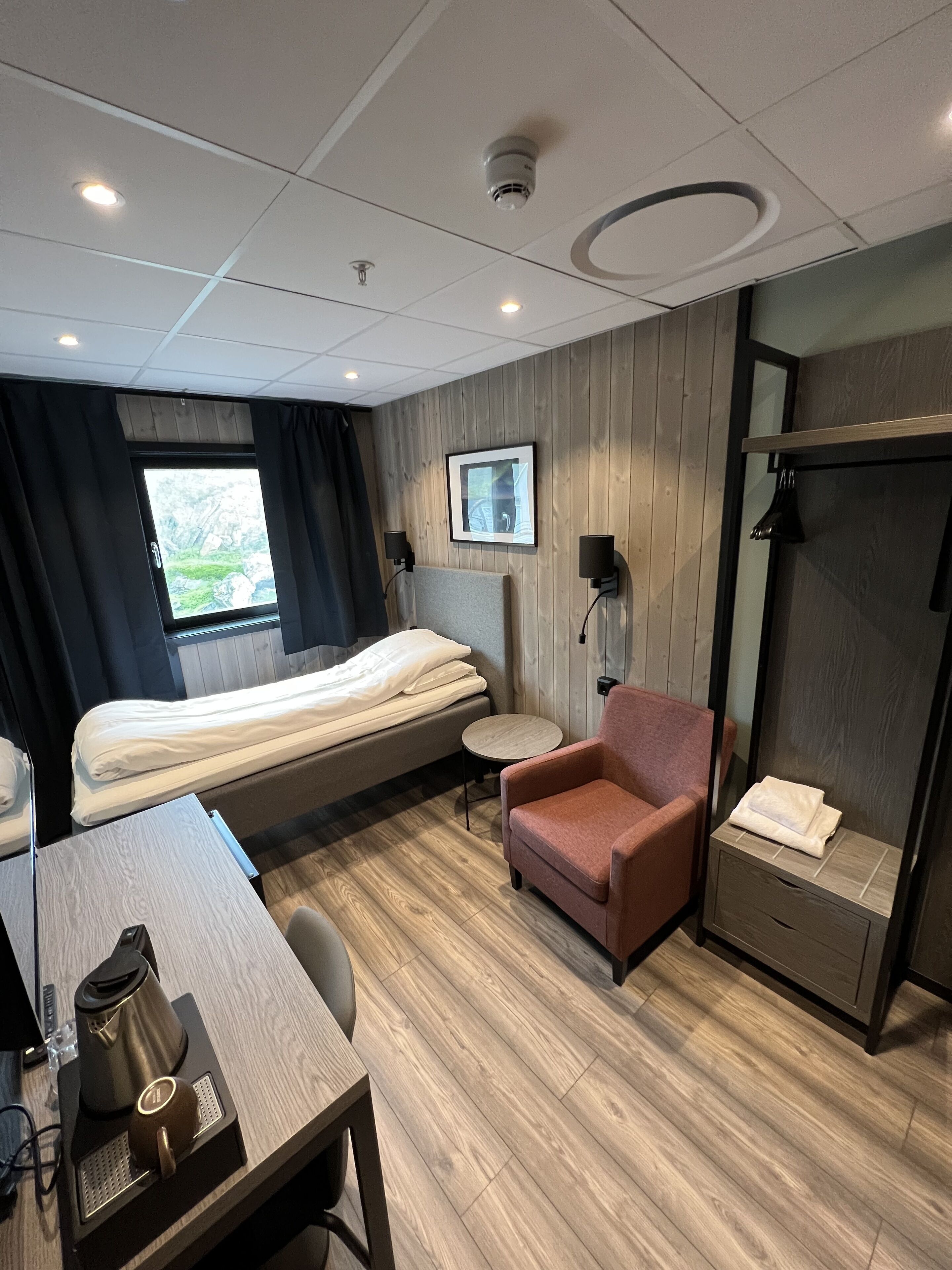 A hotel room with a bed, a desk, a chair, a TV, and a wardrobe.