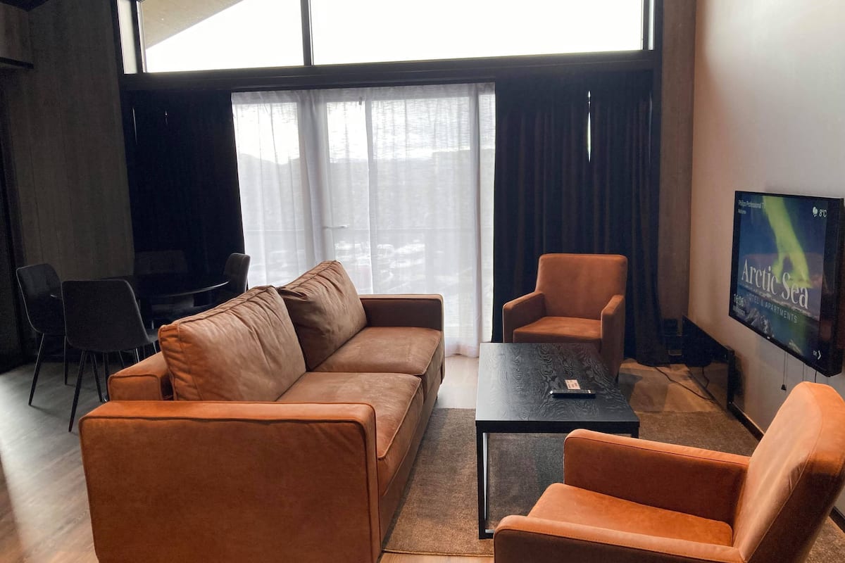 A modern living room with a brown leather sofa, a matching armchair, a coffee table, and a TV mounted on the wall.