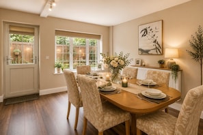 A dining room with a wooden table set for six, surrounded by patterned chairs, a vase of flowers, and candles. - Stubbs House, Loddon, sleeps 20, 2 hot tubs (Loddon)