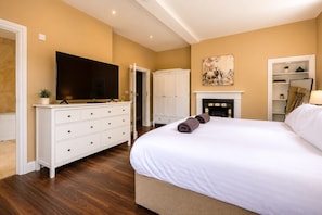 A bedroom with a bed, a TV, a dresser, a fireplace, and a painting on the wall. - Stubbs House, Loddon, sleeps 20, 2 hot tubs (Loddon)