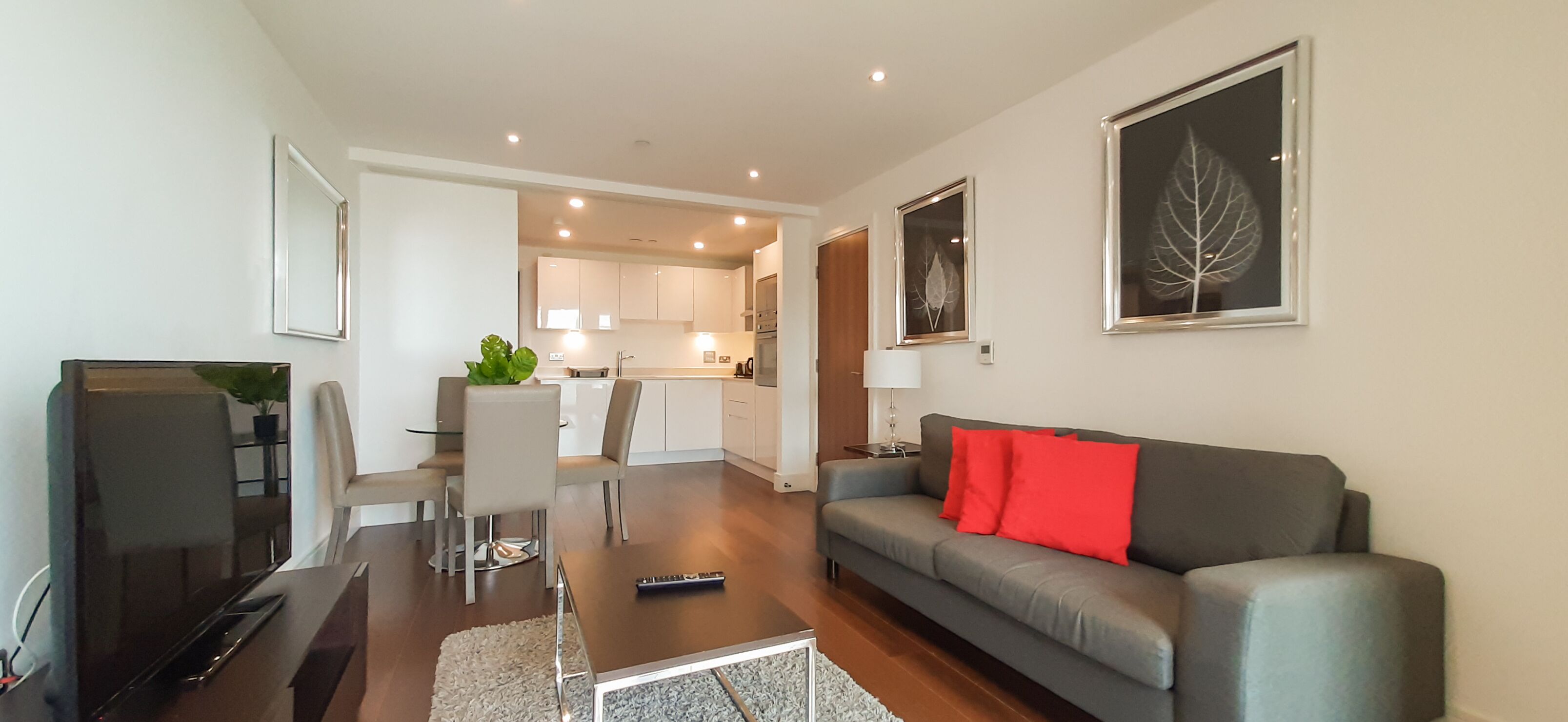 A modern living room with a grey sofa, a TV, and a dining area with a table and chairs.