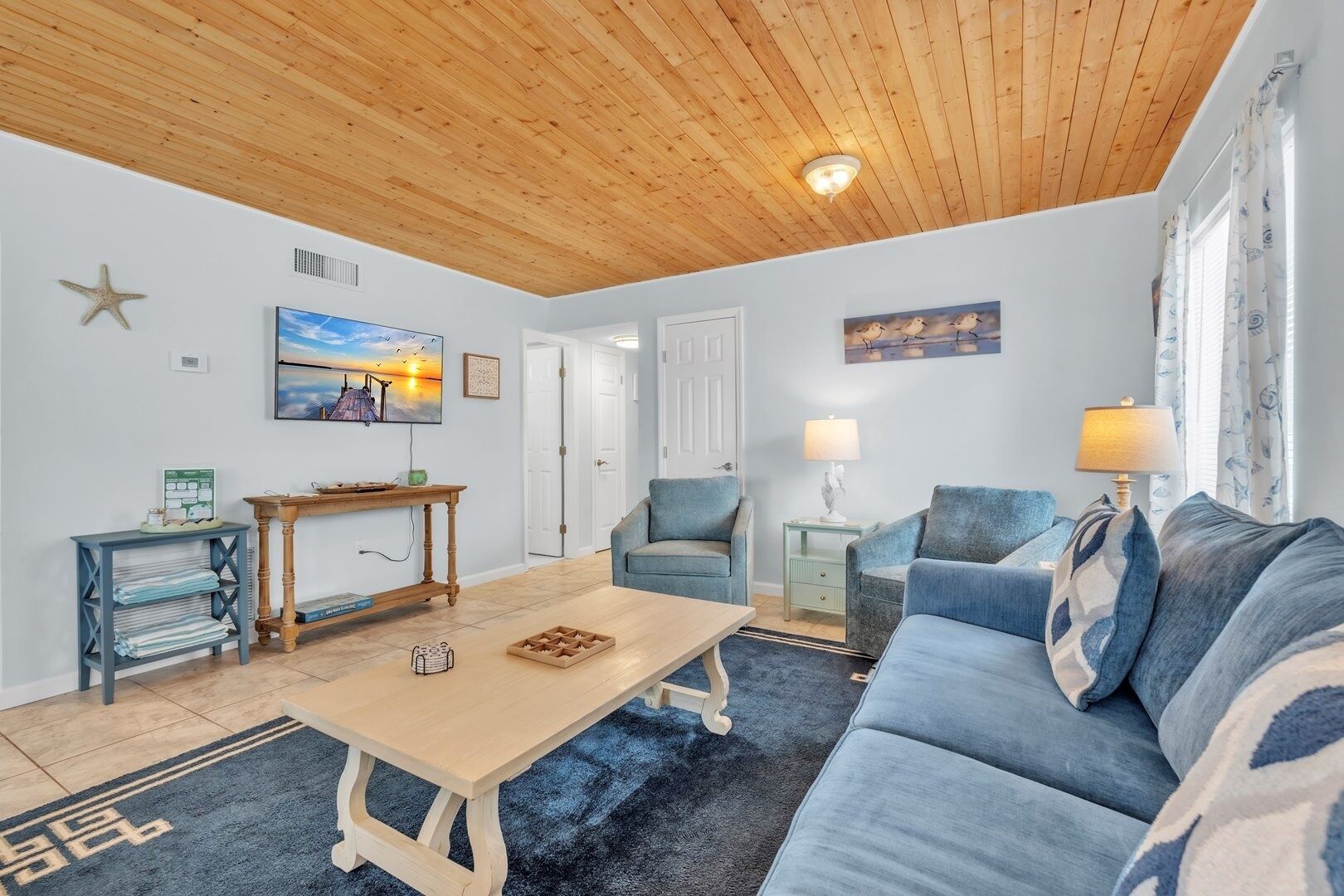 A living room with a wooden ceiling, a blue sofa, a wooden coffee table, and a TV on the wall.