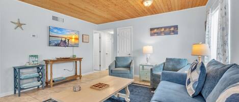 A living room with a wooden ceiling, a blue sofa, a wooden coffee table, and a TV on the wall.
