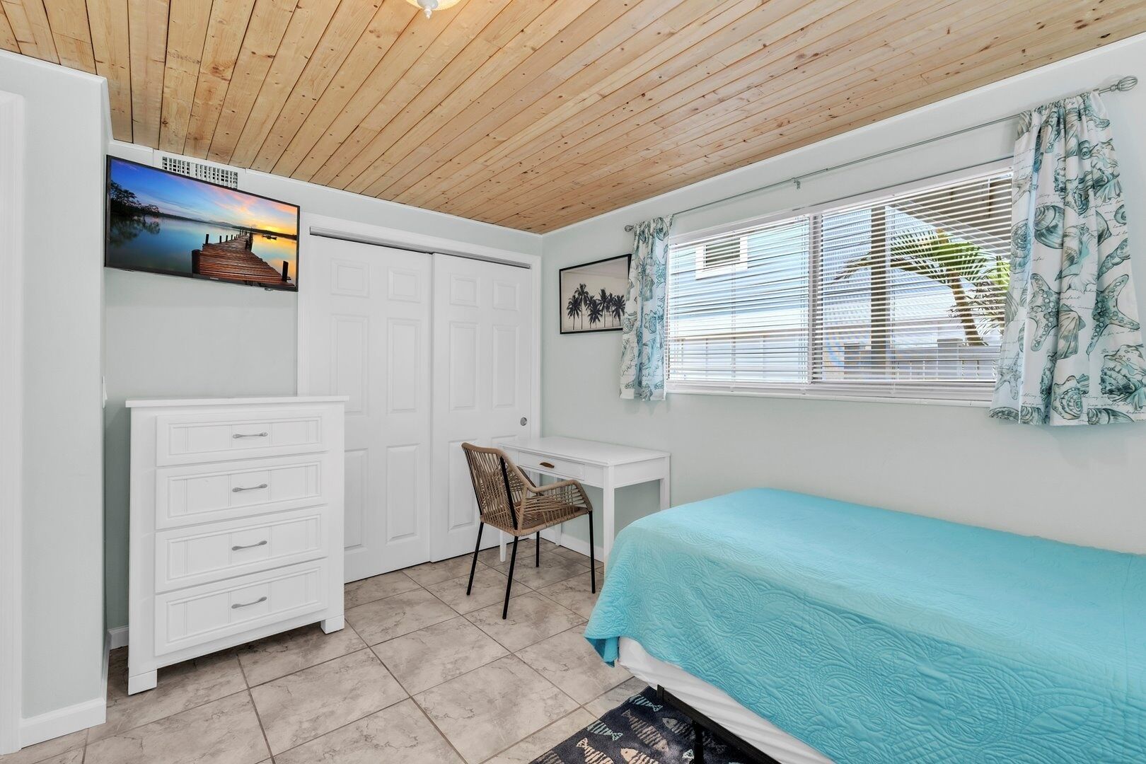 A bedroom with a bed, a desk, a chair, a wardrobe, and a window with curtains.