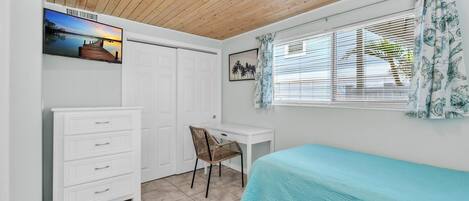 A bedroom with a bed, a desk, a chair, a wardrobe, and a window with curtains.