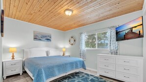 Un dormitorio con cama, mesitas de noche, cómoda, ventana con persianas, un cuadro y un tapete con forma de estrella de mar.