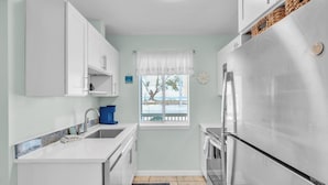 Una cocina compacta con armarios blancos, un refrigerador de acero inoxidable, una cafetera y una ventana con persianas.