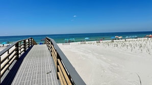 Ein Strand mit einer hölzernen Prominade, die zum Ufer führt, strahlend blauem Himmel und Meerblick.