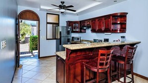 A modern kitchen with dark wood cabinets, a granite countertop, and a ceiling fan. - Guapinol 3☀Pool and AC♆ close to Beach ⛱ and Restaurant (Langosta)