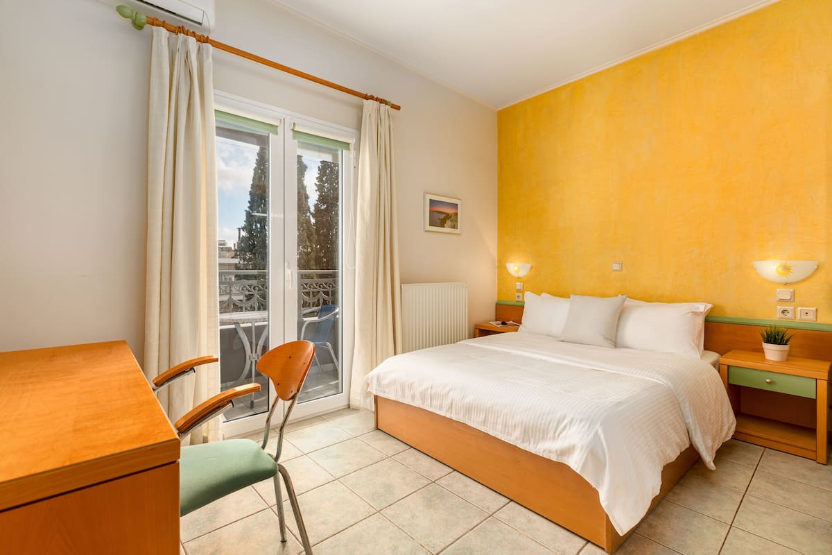 A hotel room with a bed, a desk, a chair, a nightstand, and a window with curtains.