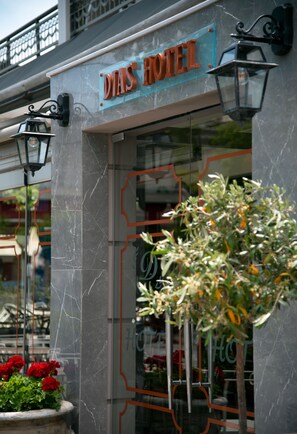 A hotel entrance with a marble facade, a sign reading "DIAS HOTEL", and a potted plant with red flowers in front. - Dias Hotel & Spa (Dio-Olympos)