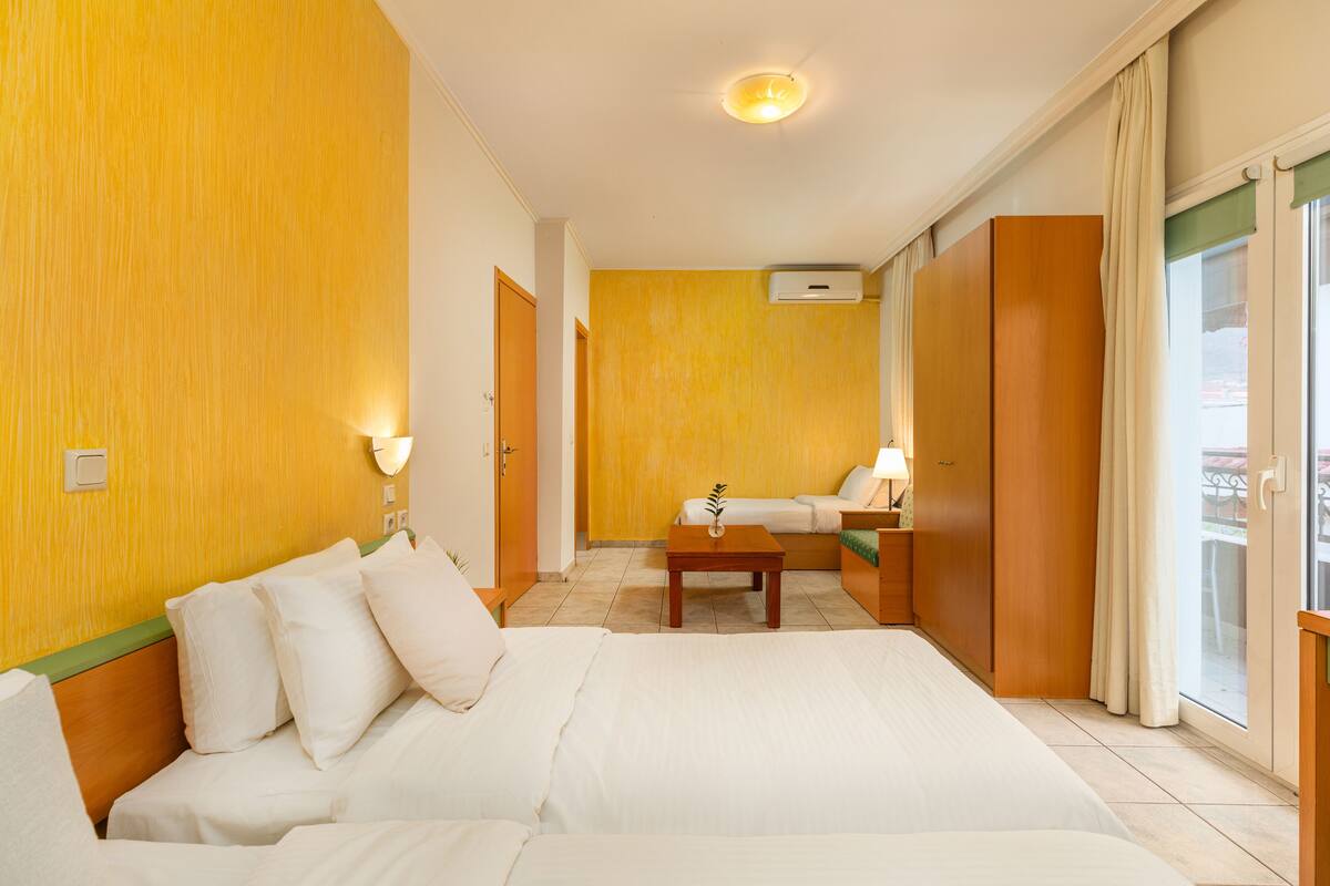 A hotel room with a large bed, a sofa, a small table, and a window with curtains.