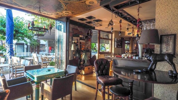 A bar area with a wooden counter, leather stools, and hanging lights. - Dias Hotel & Spa (Dio-Olympos)