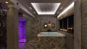 A luxurious bathroom with a freestanding bathtub, patterned tiles, a skylight, and a window with candles. - Dias Hotel & Spa (Dio-Olympos)