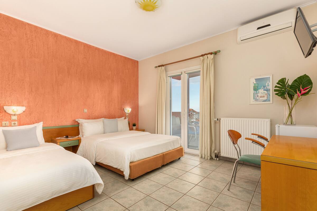 A hotel room with two beds, a desk, a chair, a radiator, and a window with curtains.