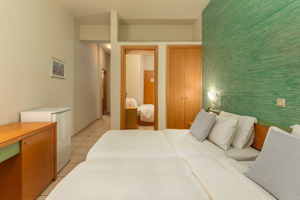 A hotel room with a bed, a desk, a refrigerator, and a green textured wall.
