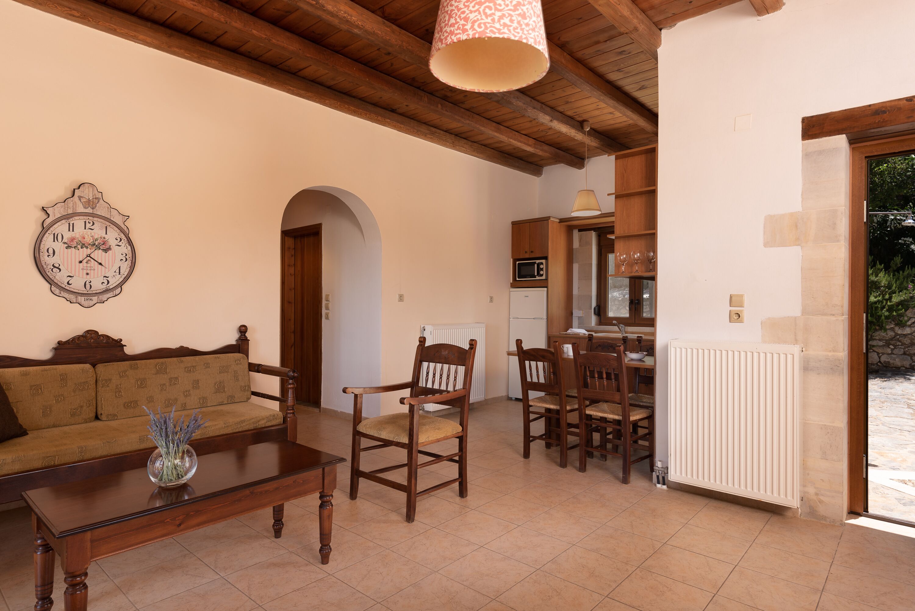 A living room with a wooden ceiling, a sofa, a coffee table with a vase, and a dining area with chairs and a table.
