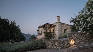 Un bâtiment en pierre avec une pergola en bois, un mur en pierre doté d’une fenêtre et une lanterne illuminée.