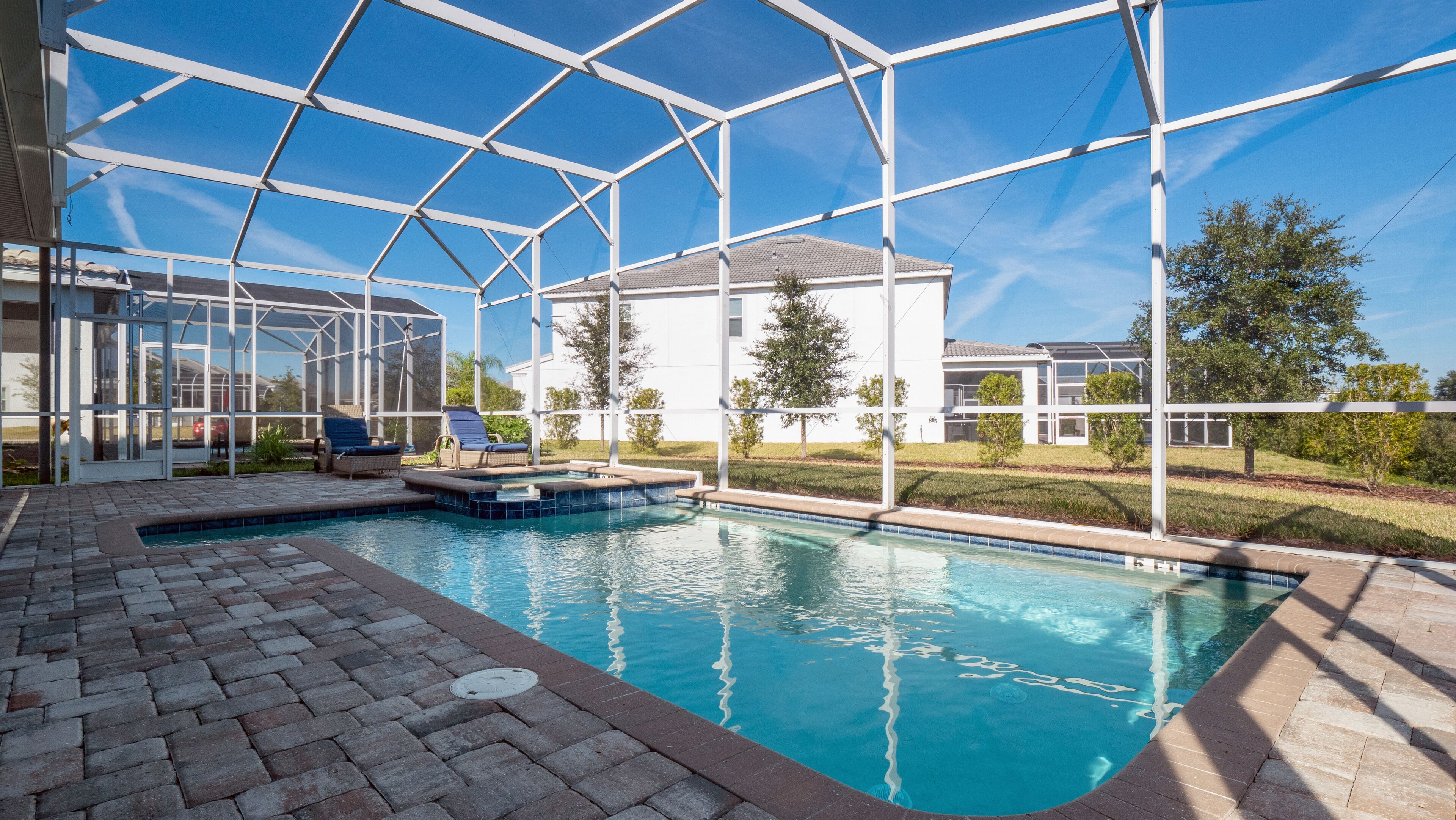 Una piscina con cerramiento de vidrio, sillas de descanso y vistas a una zona residencial.