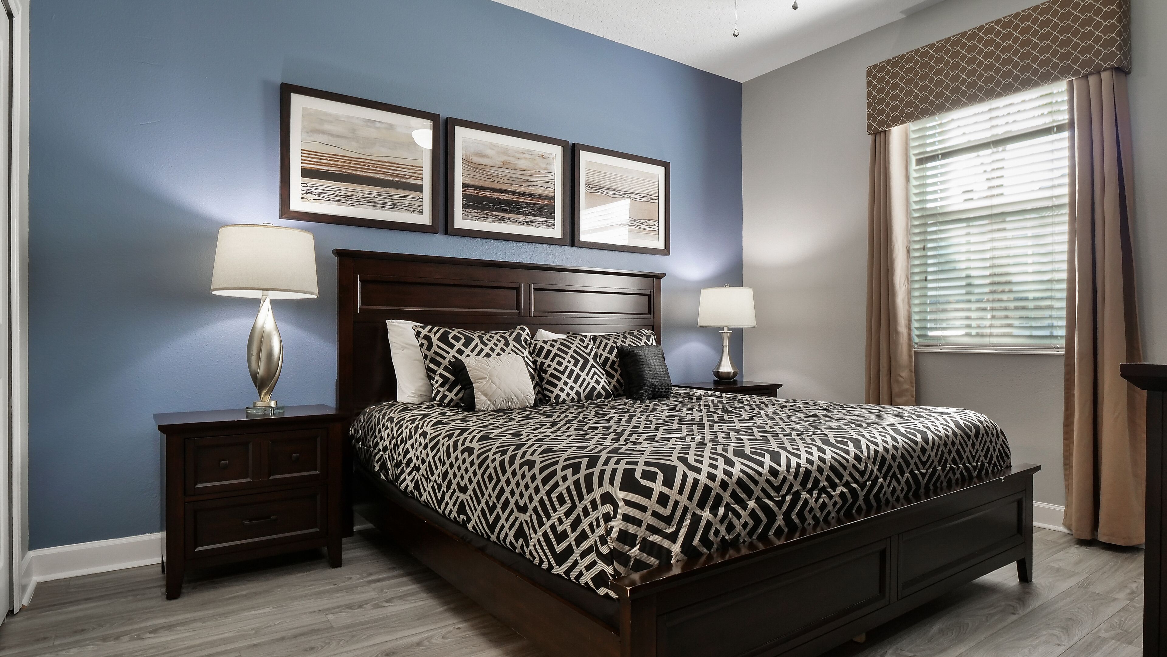 A bedroom with a dark wood bed, two nightstands with lamps, a headboard with a decorative panel, and three framed artworks on the wall.