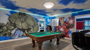 Quarto com mesa de bilhar, um grande mural do Hulk e um mural do Homem de Ferro.
