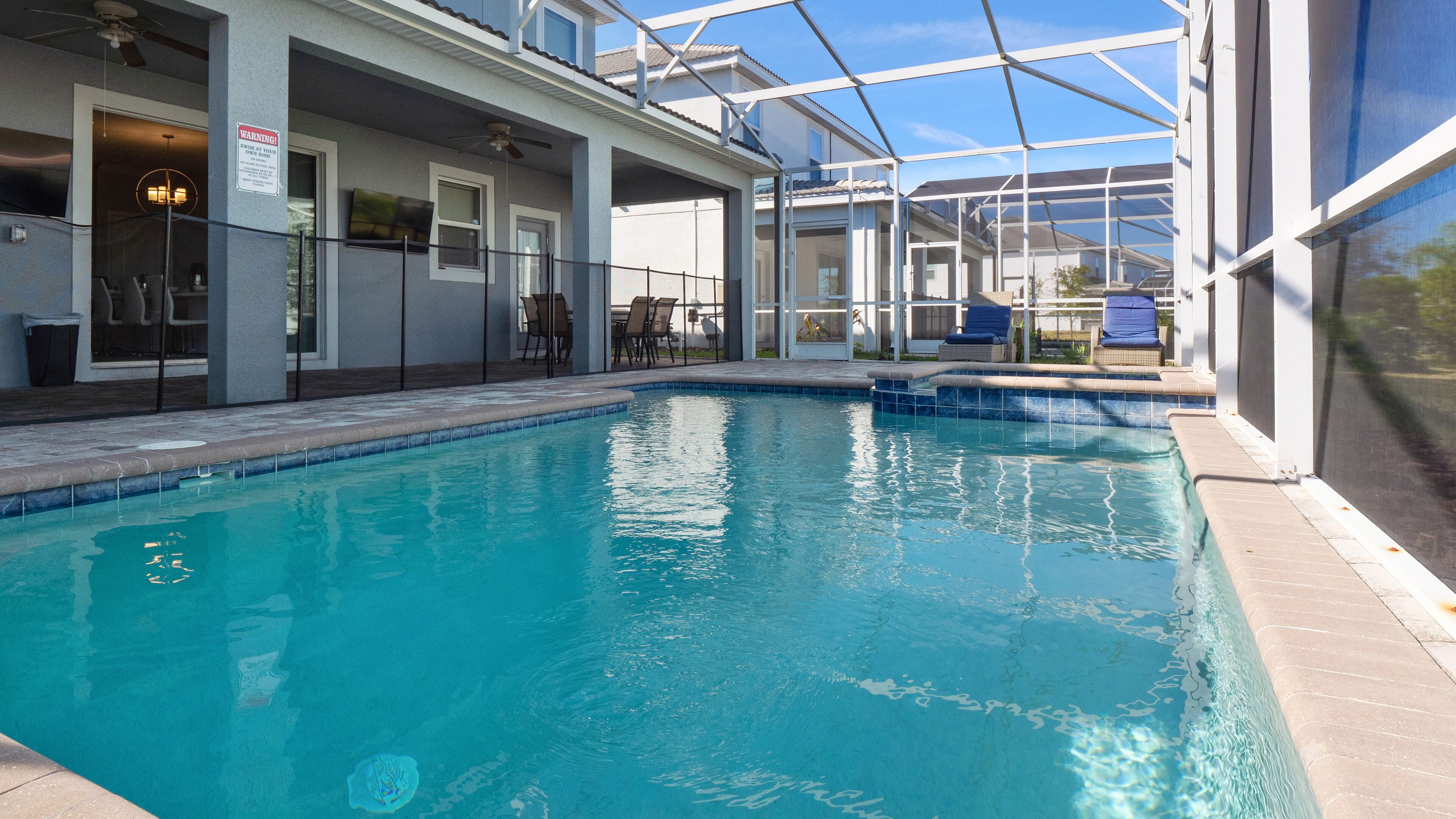 A swimming pool with a glass enclosure, outdoor seating, and a warning sign.