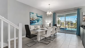 A modern dining area with a white table and chairs, a large abstract painting, and a view of a swimming pool through glass doors. - 8BR Villa,Outstanding Game Room,Resort - by Blue Sky Villas (Championsgate)