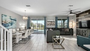 A spacious living room with a dining area, a sofa, a TV, and a ceiling fan. - 8BR Villa,Outstanding Game Room,Resort - by Blue Sky Villas (Championsgate)