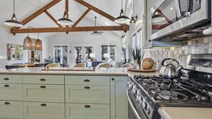 Una cocina con isla central, vigas de madera, luces colgantes, estufa y microondas.