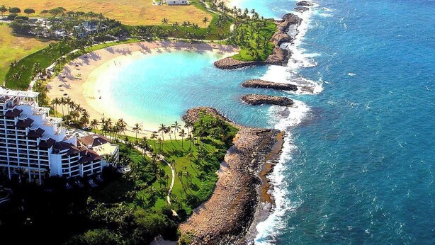 Luftaufnahme eines Küstenresorts mit mehreren Strandhäusern, einem Sandstrand und klarem, blauem Wasser.
