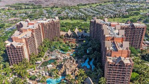 Ein Resort mit mehreren Hochhäusern, einem zentralen Poolbereich mit Palmen und einem Golfplatz im Hintergrund.