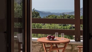 Mesa de madeira com duas maçãs e dois copos numa varanda com vista para uma paisagem montanhosa.
