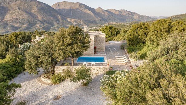 Uma área de piscina com uma estrutura de pedra, rodeada por árvores e montanhas ao fundo.