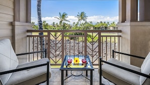 Ein Balkon mit zwei gepolsterten Stühlen und einem Tisch mit zwei Gläsern und einer gelben Blume.