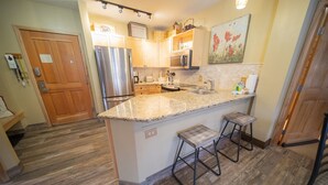 A kitchen with a granite countertop, stainless steel appliances, wooden cabinets, and a small island with stools. - Renovated Unit W/Fireplace, Walk to Restaurants. (Keystone)