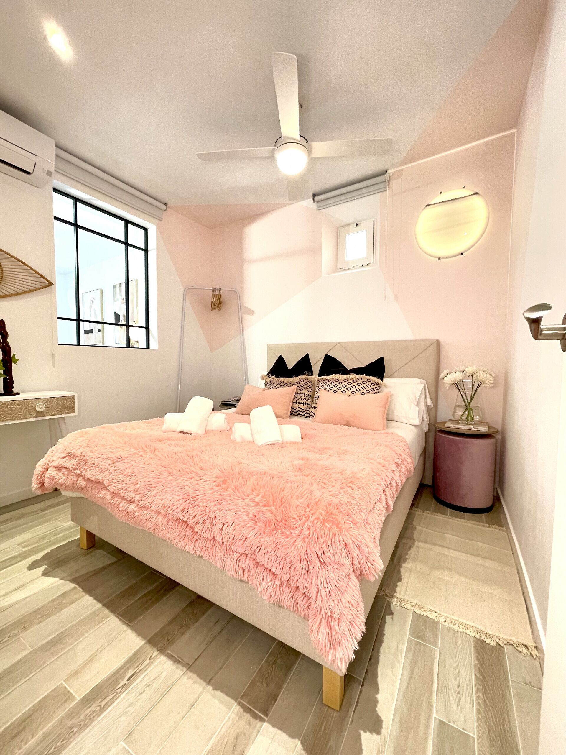 A bedroom with a bed, a ceiling fan, a window, and a bedside table with a vase.