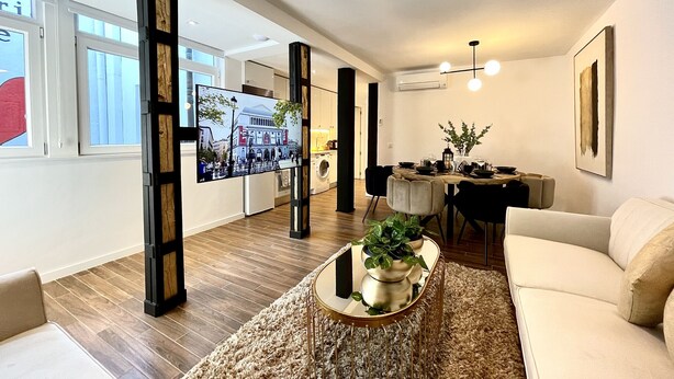 Un salon moderne comprenant un canapé, une table basse avec une plante, un coin repas avec une table et des chaises, et un téléviseur fixé sur une structure en bois.