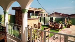 A covered outdoor area with a wooden deck, a brick structure, and a green fence. - Spacious 5 BR Villa with amazing views Bar&Pool | family & large groups | Wi-Fi (Accra)