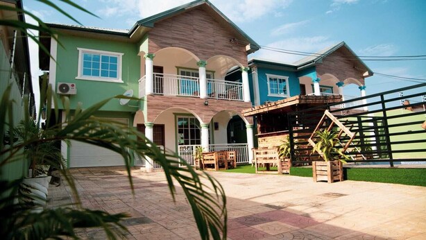 A two-story house with a balcony, a wooden deck, and a fenced area with plants. - Spacious 5 BR Villa with amazing views Bar&Pool | family & large groups | Wi-Fi (Accra)