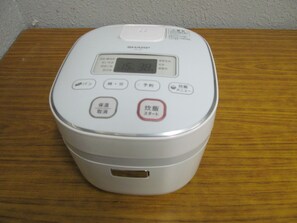 A white rice cooker with a digital display on a wooden table.