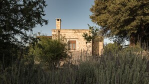 A stone building with a chimney, surrounded by trees and tall grasses. - Koules Estate-Helianthus, with Pool & BBQ,an Agricultural barn for Nature lovers (Rethymno)