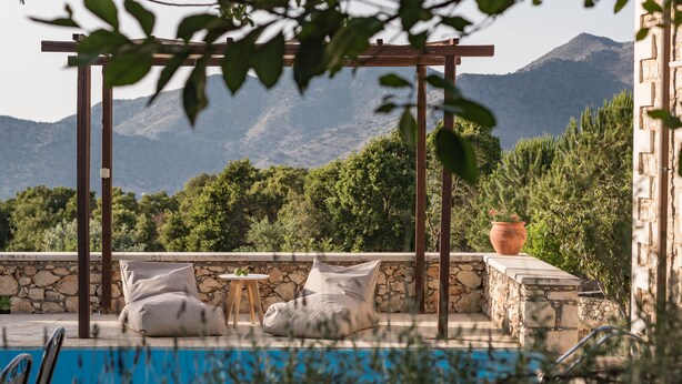 A poolside area with a pergola, two bean bags, a stone wall, and a view of mountains. - Koules Estate-Helianthus, with Pool & BBQ,an Agricultural barn for Nature lovers (Rethymno)