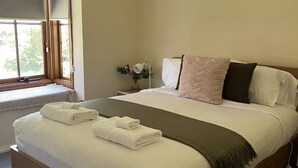 Uma cama bem arrumada com almofadas e um cobertor, uma mesa de cabeceira com abajur e uma janela com persianas.
