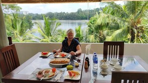 Une table à manger dressée, avec un repas, donnant sur un lac et bordée de palmiers.